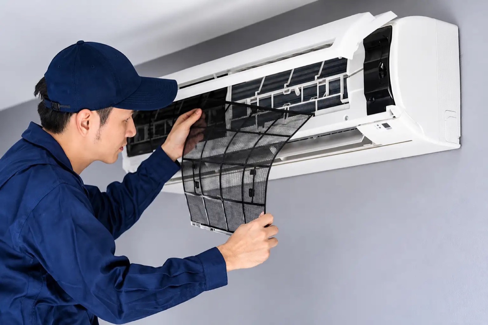 A technician in a cap removing the filter from a wall-mounted indoor air conditioning unit