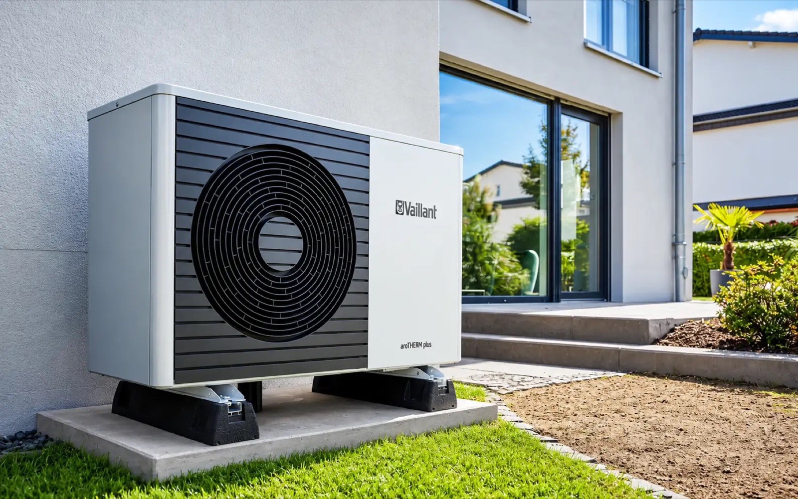A white heat pump outdoor unit on a stand beside a house with a garden