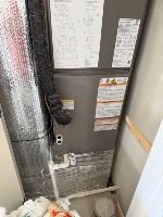 An indoor air handler unit with warning labels and flexible ductwork in an equipment closet