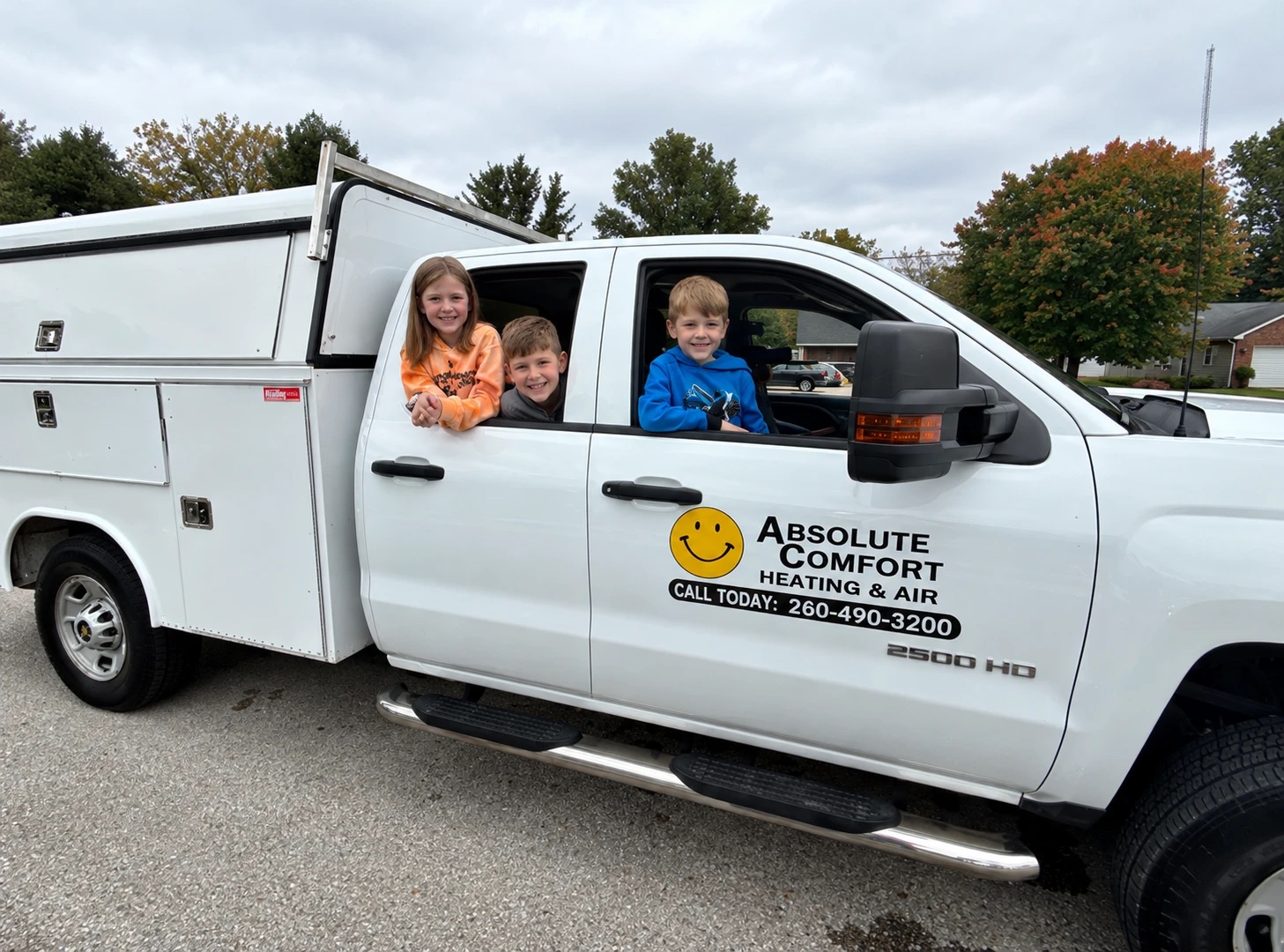 Three children sitting in the cab of a white Absolute Comfort Heating & Air work truck